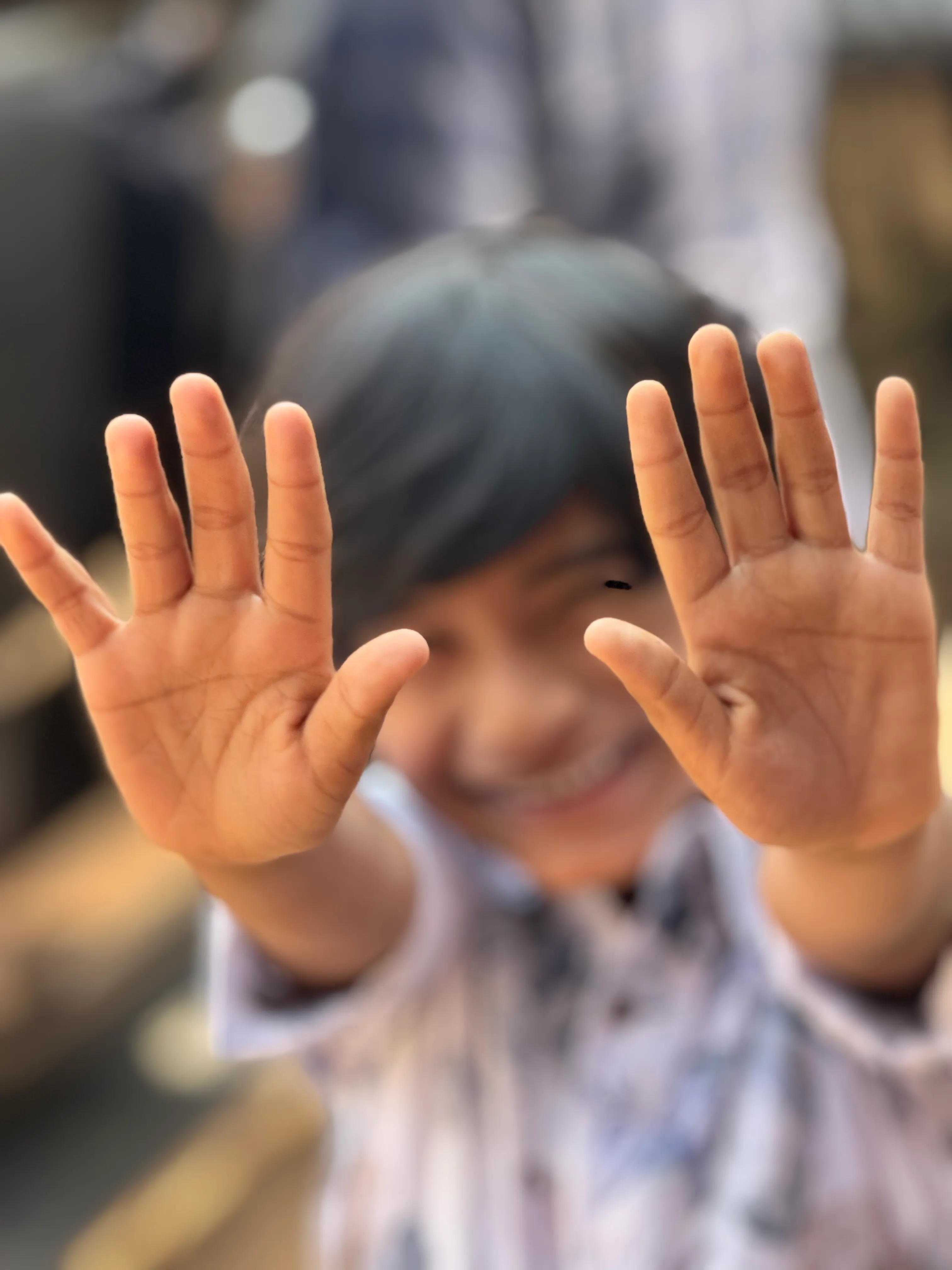 A smiling child reaching both open hands toward the camera.