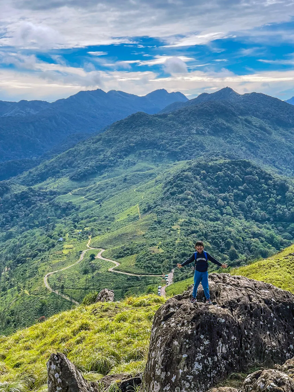 A child standing on a summit with arms open to the mountains.