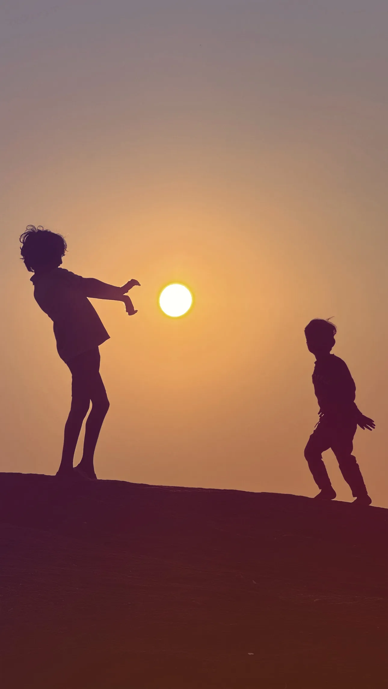 Two children playing in silhouette against a glowing sunset.